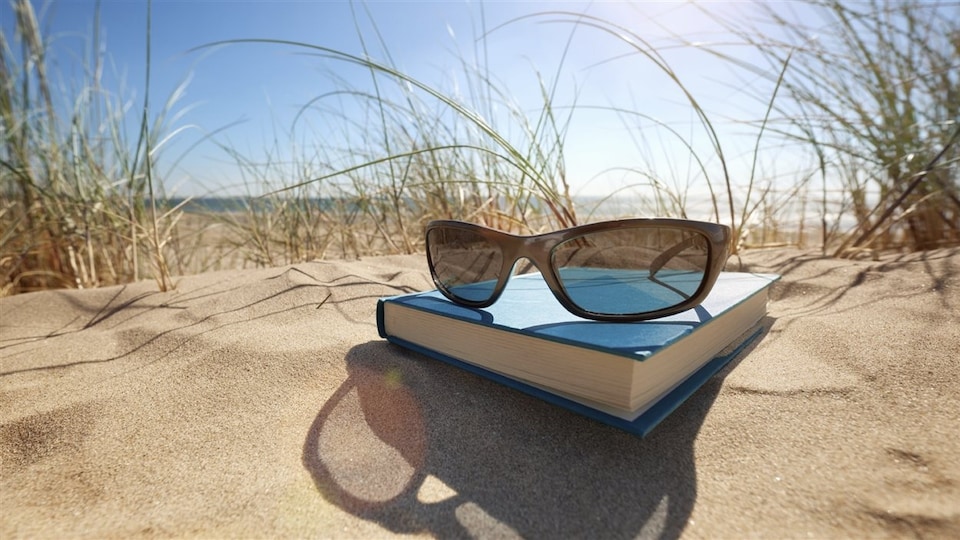 Une paire de lunette de soleil et un livre sur le sable d'une plage ensoleillée.