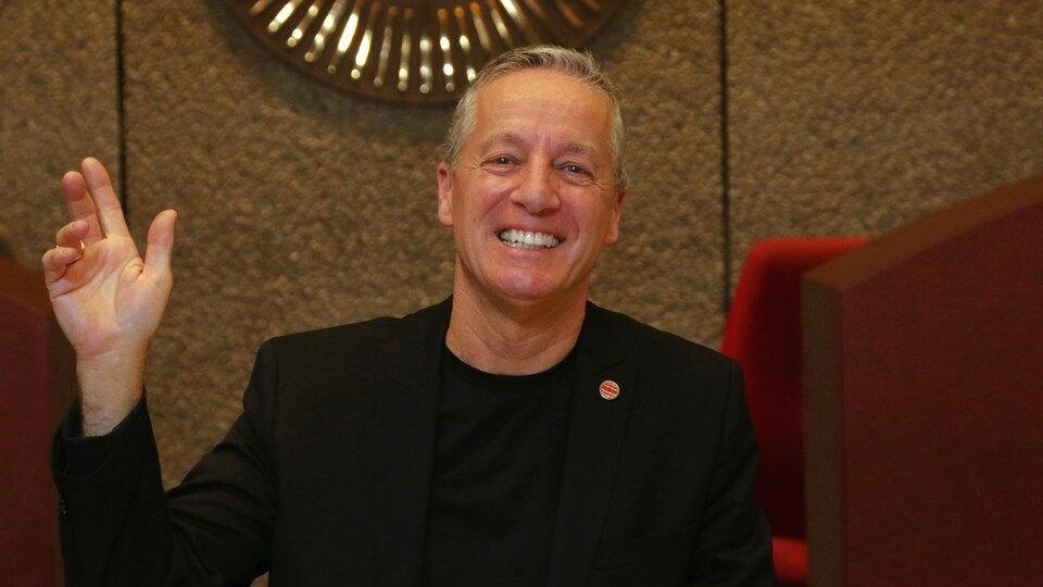 Robert Houle souriant fait un salut de la main dans le hall d'accueil de la Maison de Radio-Canada, à Montréal.