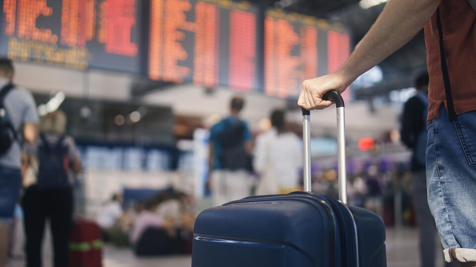 Un homme est à l'aéroport et tient sa valise avec sa main.