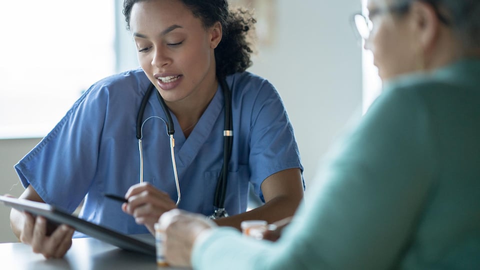Une infirmière, tablette à la main, parle avec une patiente.