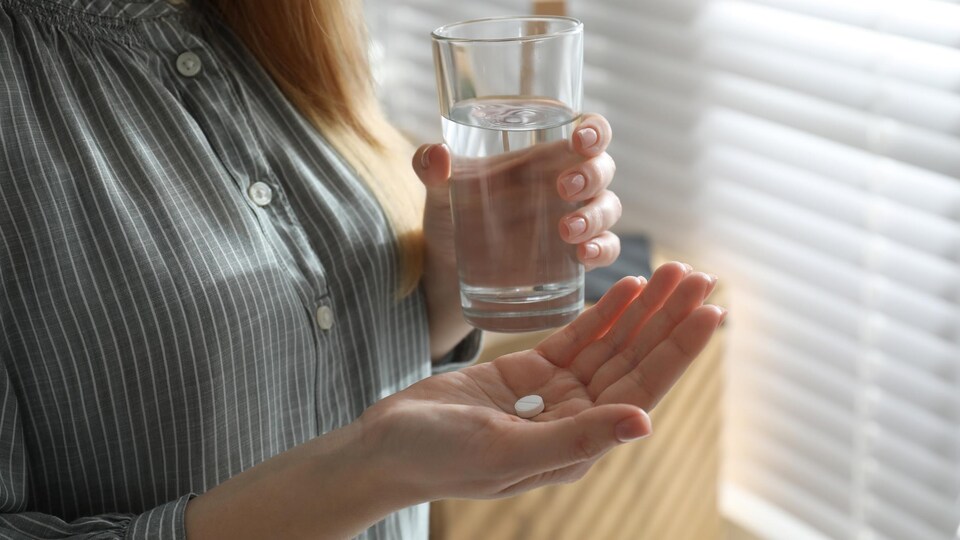 Photo d'une femme tenant une pilule et un verre d'eau.