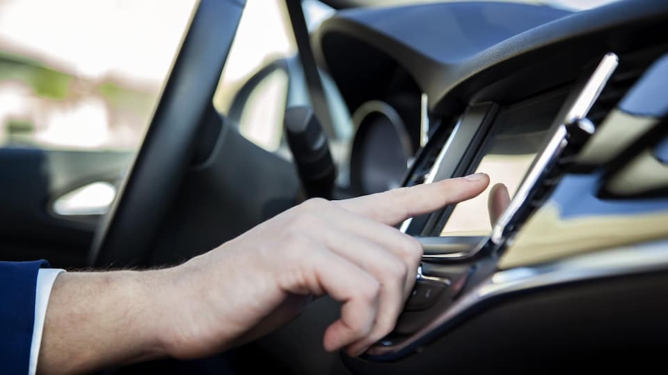 Une personne touche un écran tactile dans sa voiture.
