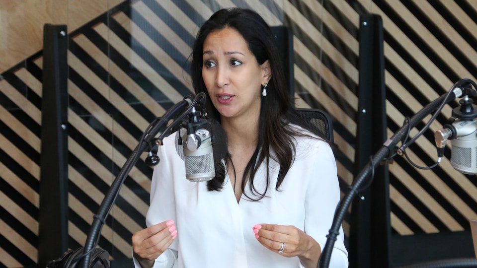 Une femme au regard inquiet parle au micro dans un studio de radio.