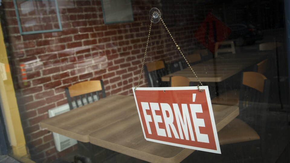 Une pancarte sur laquelle est écrit Fermé, accrochée à la vitre d'un restaurant.