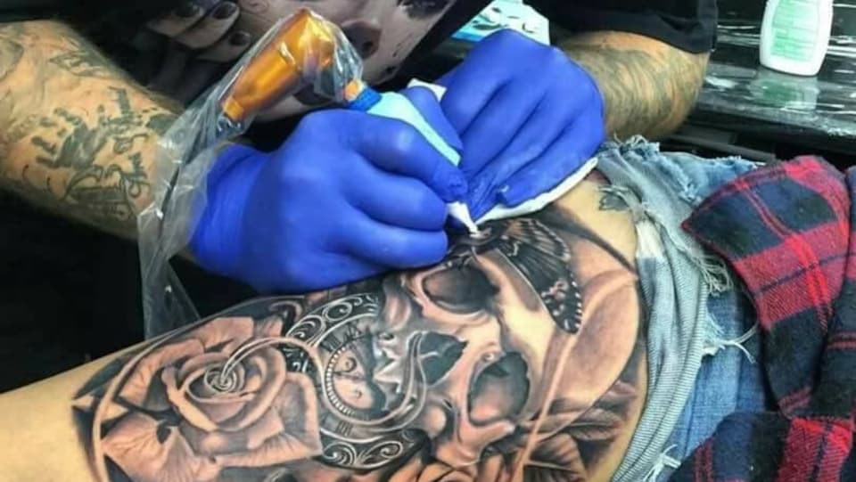 Un homme tatoue une tête de mort.