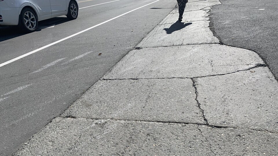 Une femme marche sur le trottoir. Une ligne peinte au sol protège les cyclistes et une voiture roule dans la rue.