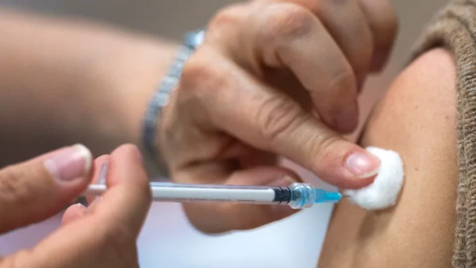 Un professionnel de la santé, dont on ne voit que les mains, administre un vaccin à un patient, dont on voit l'épaule.