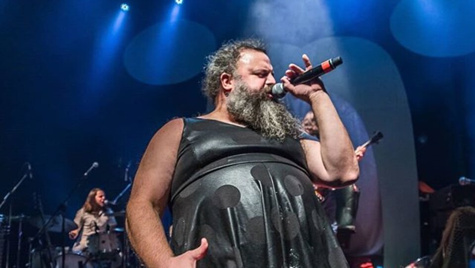 Un homme vêtu d'une robe noire en cuir chante sur scène.