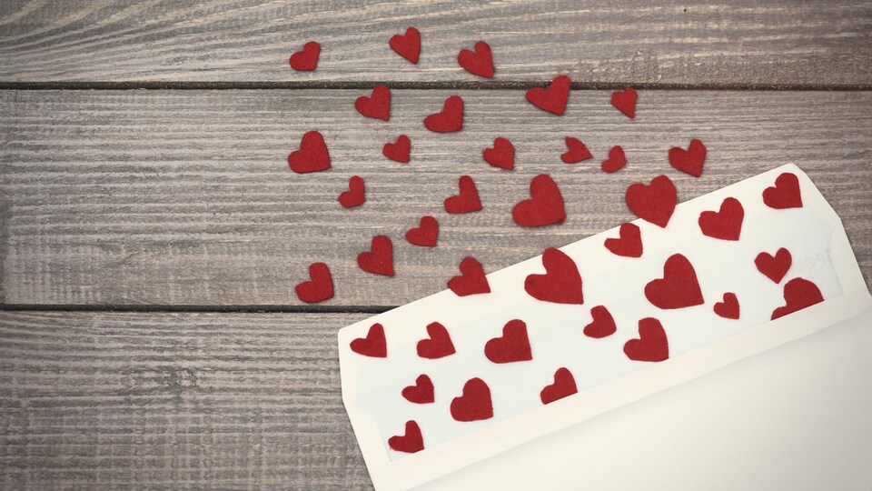 Des petits cœurs en papier rouge sortent d'une enveloppe blanche.