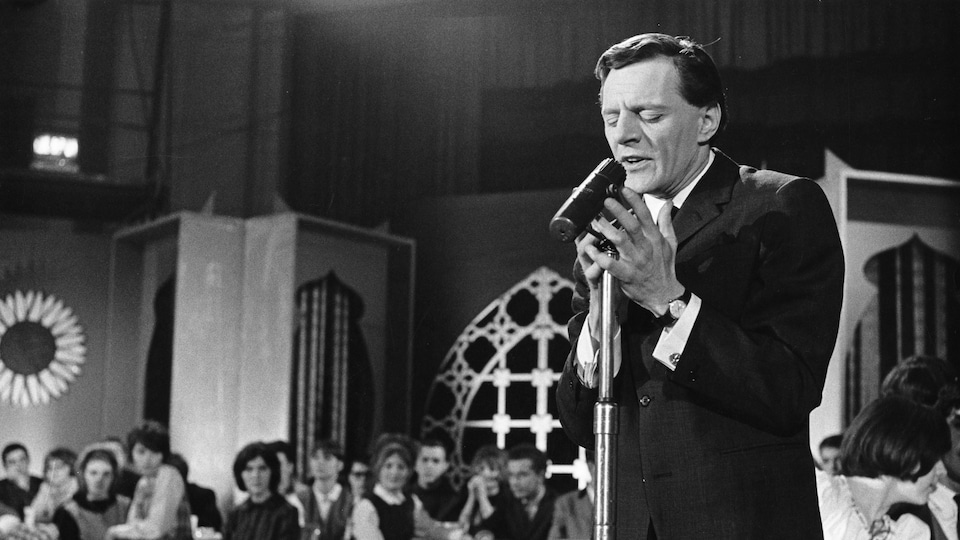 Claude Léveillée chante avec intensité debout dans une salle de spectacle en 1964.