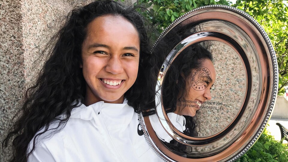 La jeune femme aux cheveux frisés sourit à pleines dents, le trophée à la main.