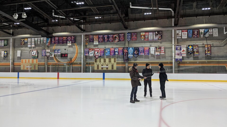 Sur une patinoire, un technicien tient un micro-perche entre un homme et une femme, les deux sur patins, qui discutent.