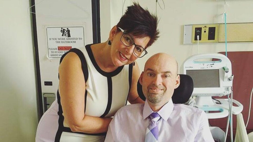 Lise Michaud derrière son frère Eddy Lefrançois, en fauteuil roulant, prêts à quitter une chambre d'hôpital vêtus de beaux vêtements.