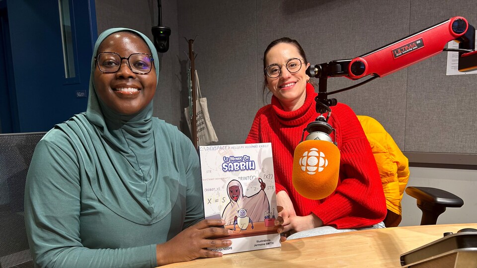 L'autrice Khadydja Ndoye présente, le sourire aux lèvres,  son livre Le Monde de Sabbih, qu'elle tient de ses deux mains, aux côtés de l'animatrice Gabrielle Sabourin lors de son passage en studio à l'émission de radio À échelle humaine.