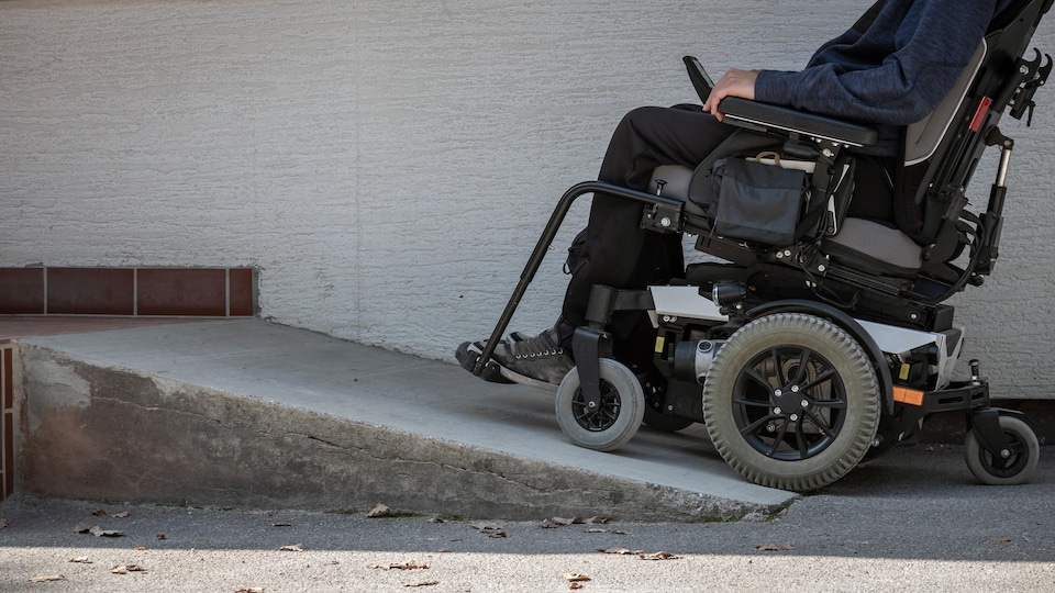 Une personne en fauteuil roulant, dans une pente pour entrer dans un bâtiment.