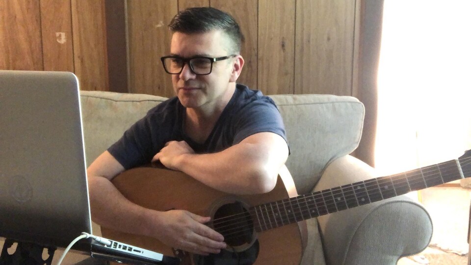 Le chanteur de Vancouver, Loig Morin, assis devant son ordinateur avec une guitare pendant le confinement chez lui