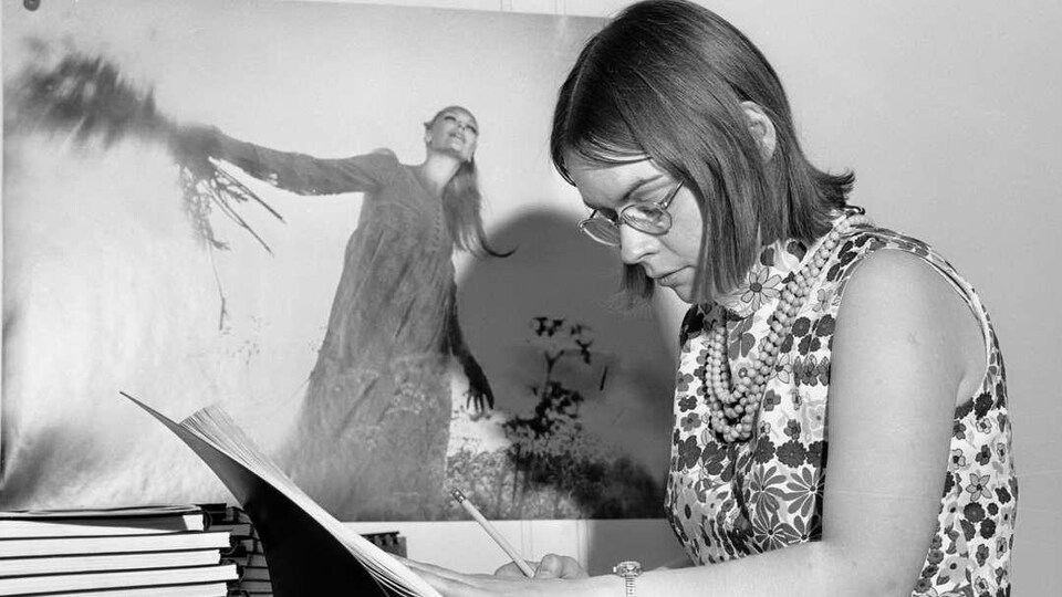 Photo en noir et blanc montrant une jeune femme en train d'écrire dans un grand livre.