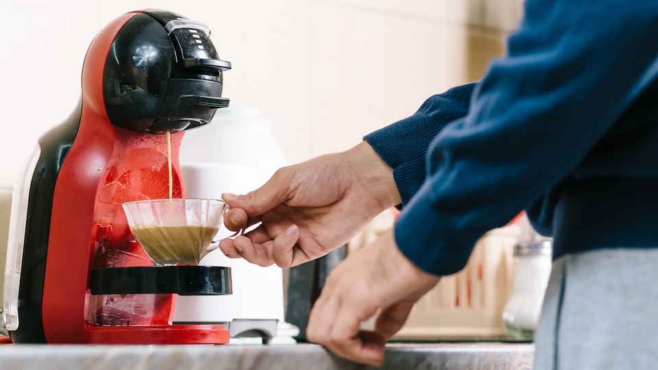 Une personne tient une tasse transparente dans laquelle du café provenant d'une machine tombe.