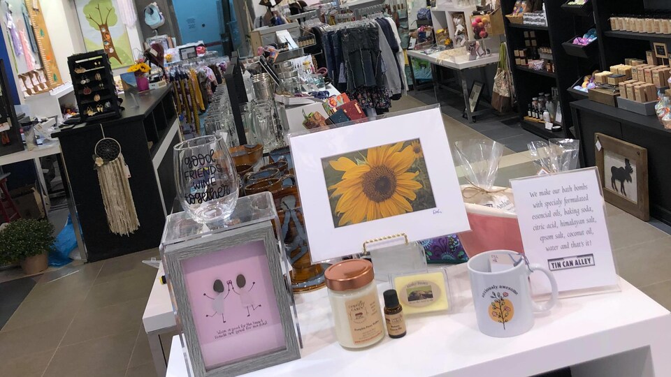 On aperçoit le magasin et les articles qui y sont en vente : chandelles, savons, cadres, décorations de maison, verres à vin, vêtements et bijoux.