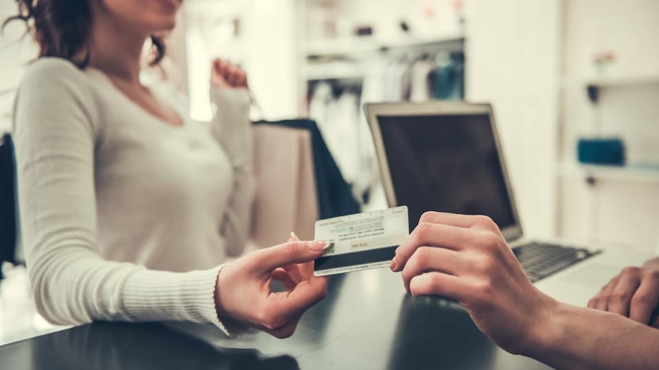 Une personne utilise sa carte de crédit pour payer à la caisse d'un magasin de vêtements.