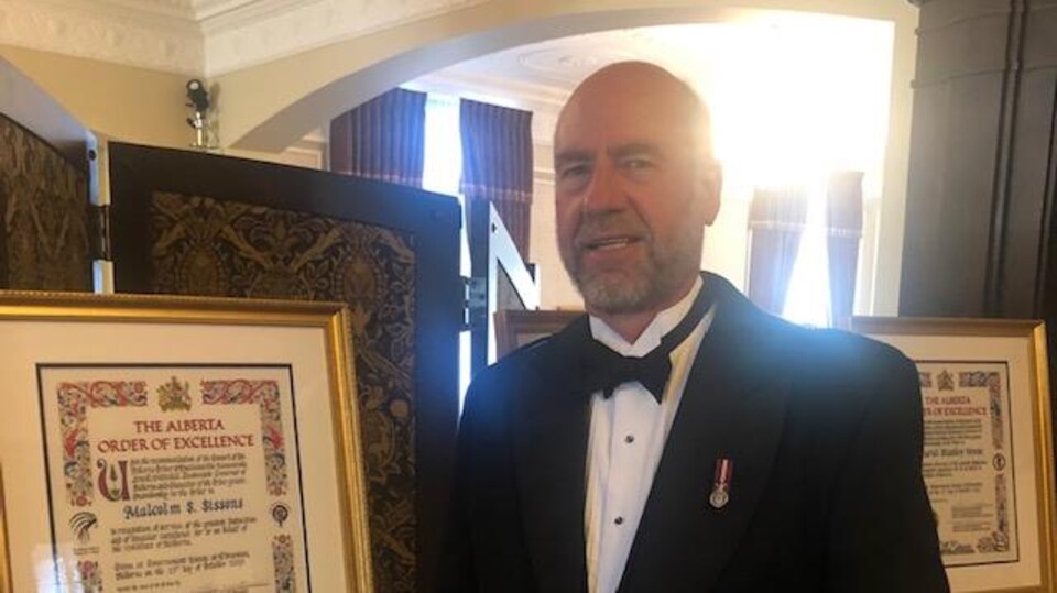 Un homme en kilt et en veston debout à côté d'un document officiel encadré