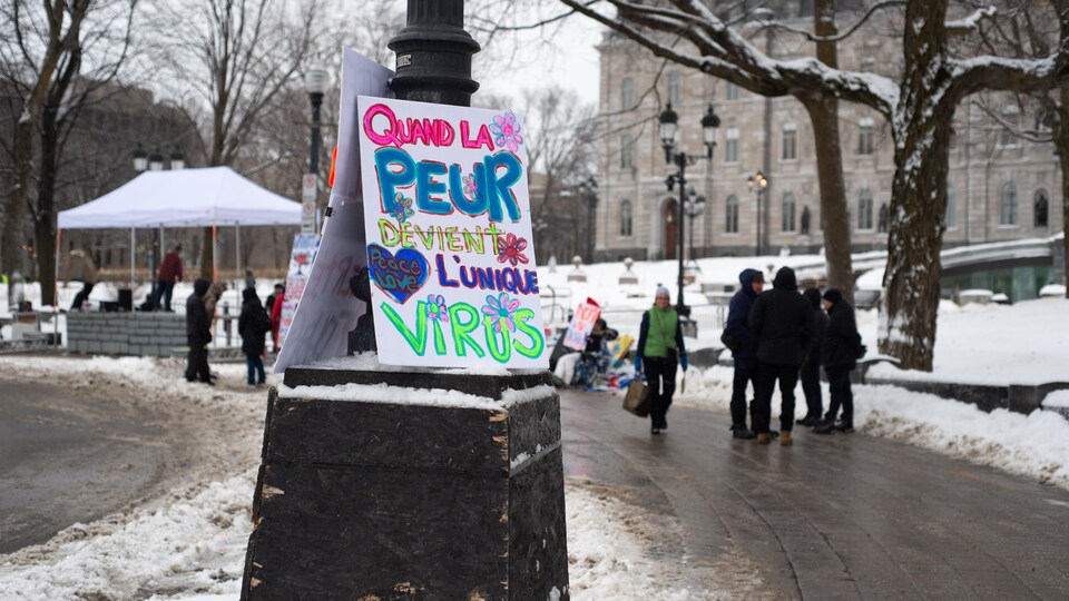 Une pancarte sur laquelle est écrit « Quand la peur devient l'unique virus » repose sur un lampadaire non loin de la fontaine de Tourny, devant l'édifice de l'Assemblée nationale du Québec.  