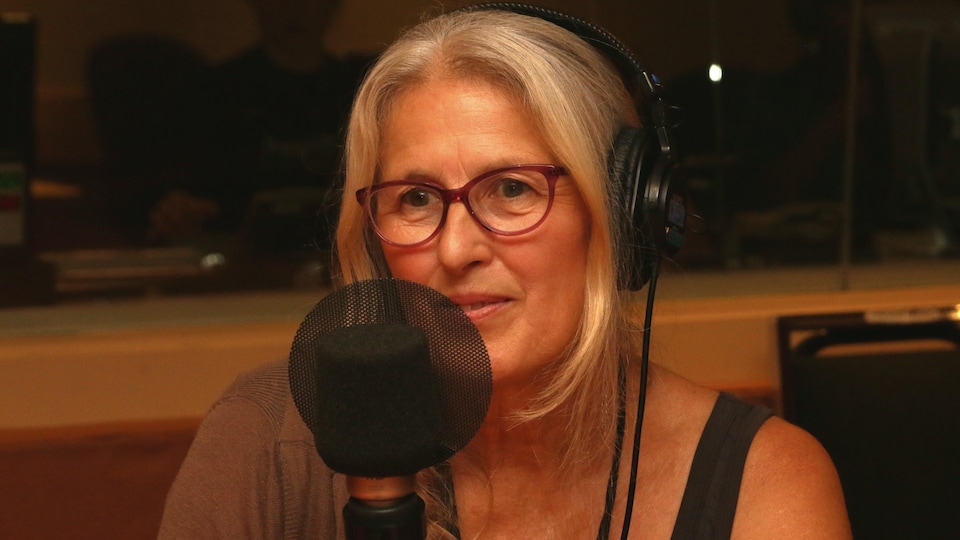Margie Gillis devant un micro de radio et un casque d'écoute sur la tête dans un studio de radio.