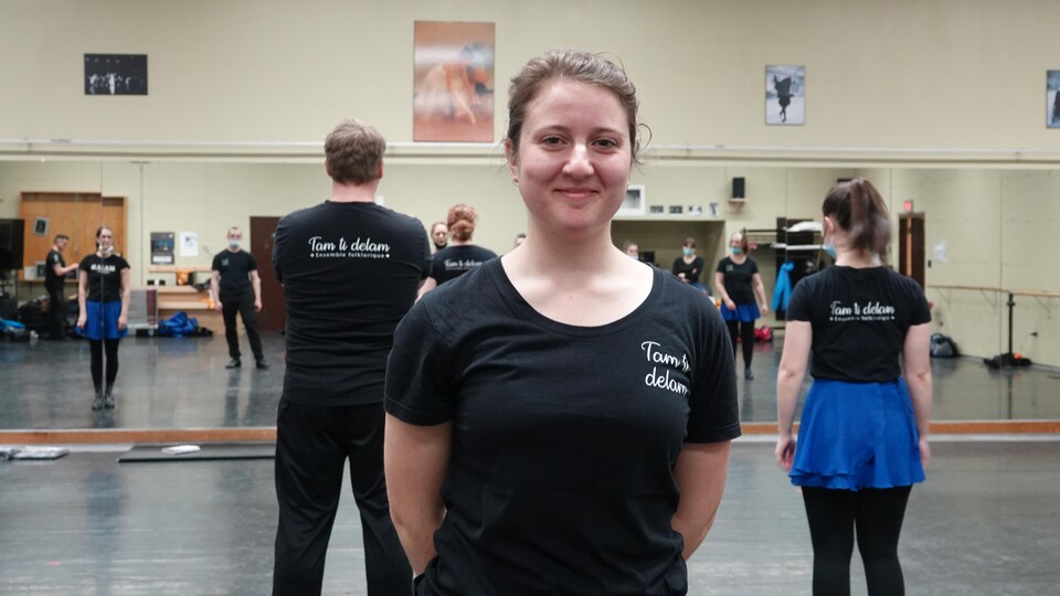 Une danseuse sourit à la caméra dans un studio de danse. 