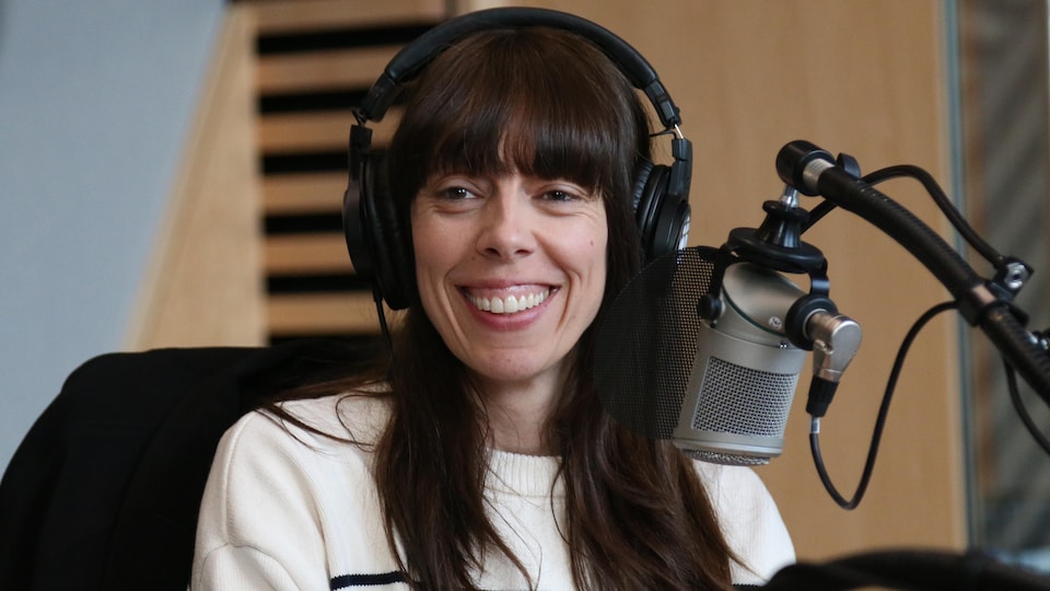 Une femme avec des écouteurs sur la tête sourit derrière un micro dans un studio de radio. 