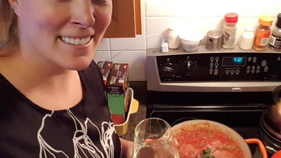 Une femme devant une sauce à spaghetti qui cuit sur la cuisinière, un verre de vin à la main.