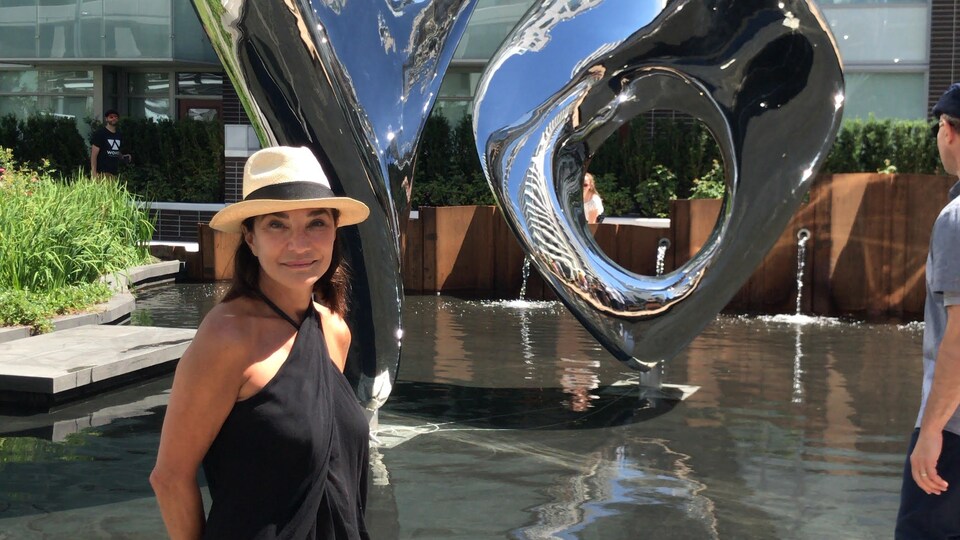 Une femme est posée debout à l'extérieur. à côté de sa sculpture.