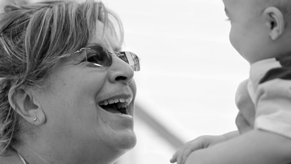 Une femme souriante qui tient un bébé à la hauteur de son visage.