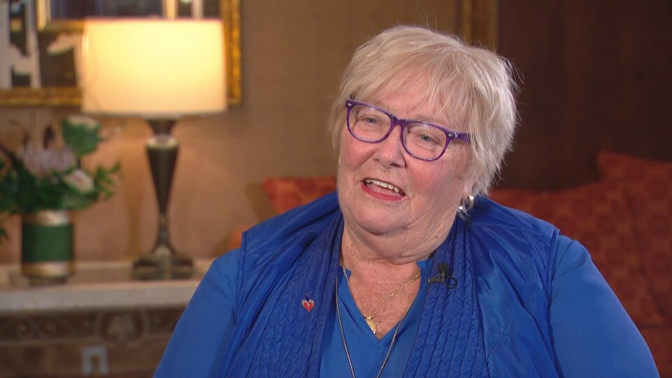 Martine Galibois-Barss est assise sur une chaise avec des coussins rouges et une lampe en arrière-plan.