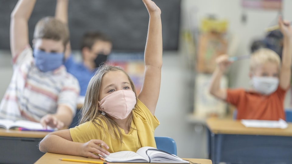 Des élèves masqués lèvent la main dans une salle de classe.