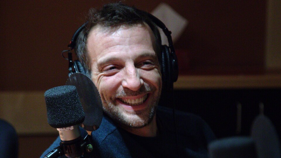Mathieu Kassovitz, des écouteurs sur la tête, est assis derrière un micro.