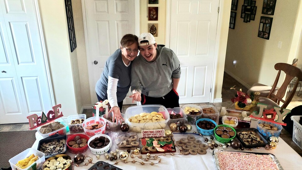 Carey Roy et son petit-fils Connor Lafortune posent fièrement devant une table remplie de biscuits et de pâtisseries.