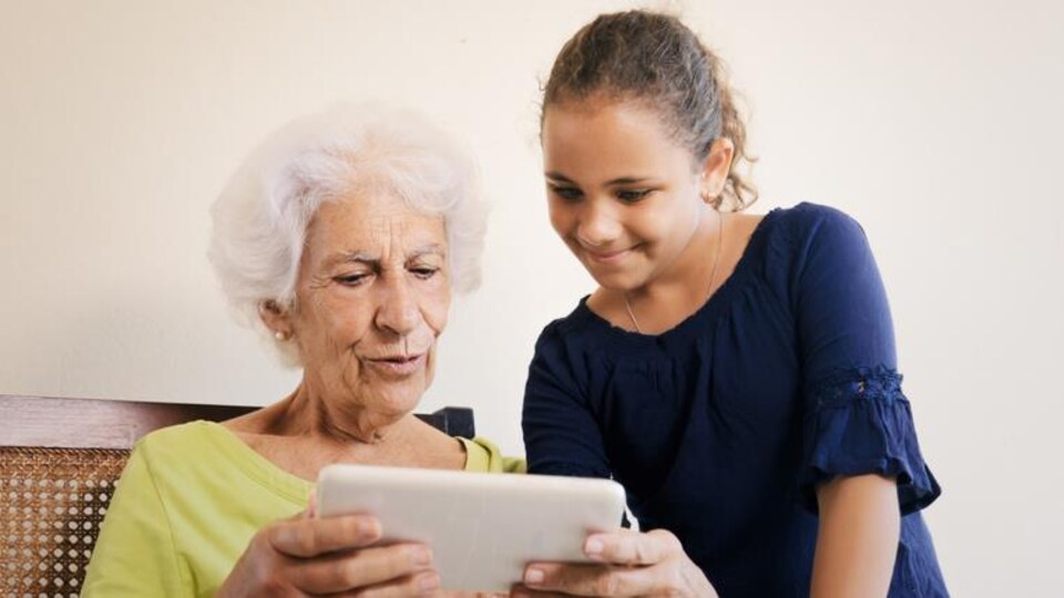 Une adolescente explique le fonctionnement d'une tablette à une aînée.