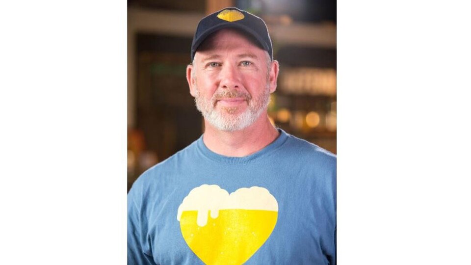 Portrait de Christo Brock, il porte une casquette et un tee-shirt à l'effigie du logo du film : un bock de bière en forme de cœur.