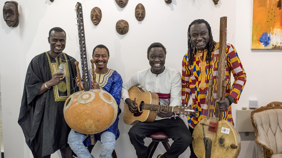 Les quatre musiciens sont devant un mur décoré de masques avec leurs instruments.