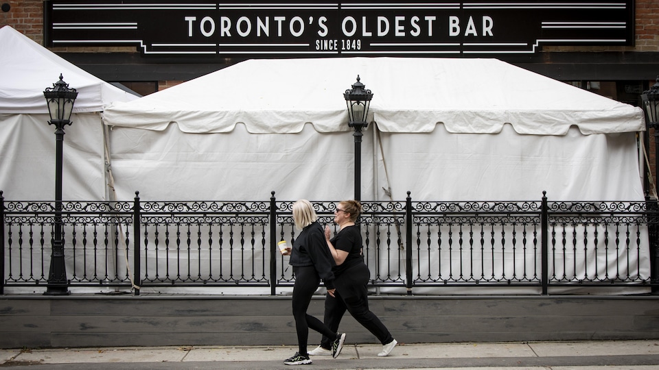 Deux femmes marchent devant un bar de Toronto dont la terrasse a été couverte.