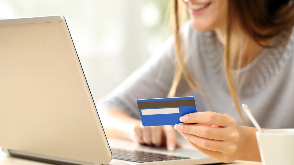 Une jeune femme effectue un achat en ligne avec son ordinateur portable et sa carte de crédit.