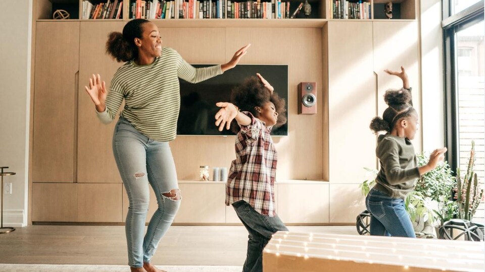 Un mère danse avec ses deux filles dans un salon.