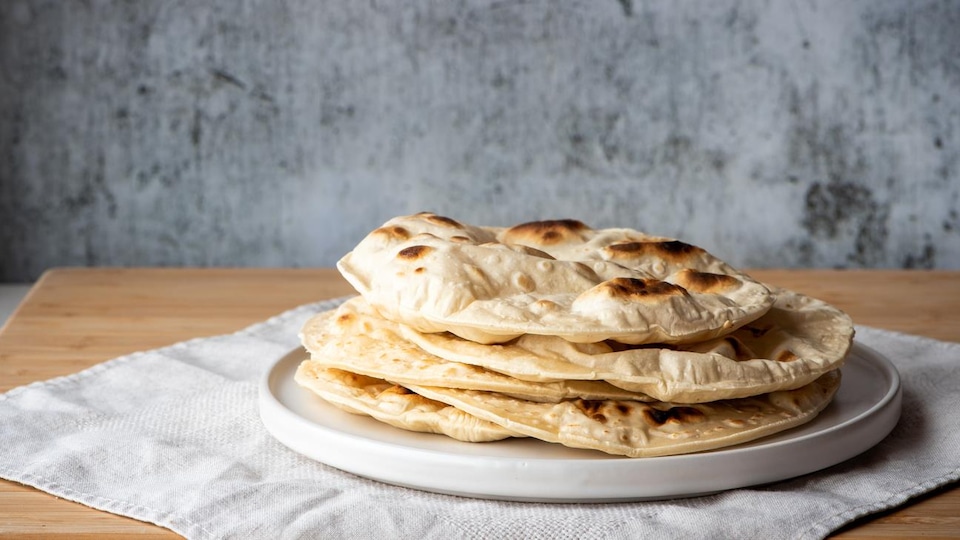 Des pains naan dans une assiette déposée sur un napperon blanc.