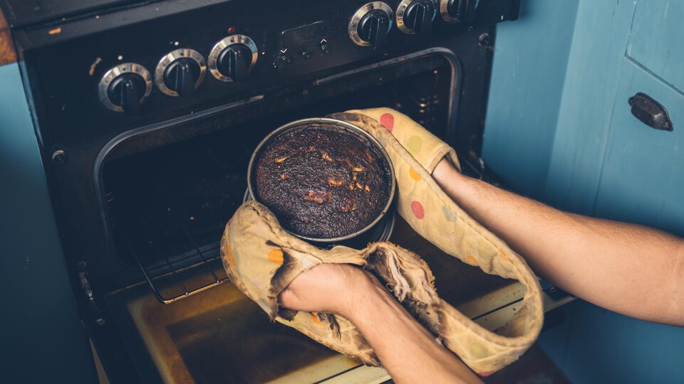 Les mains d'un homme qui retire un gâteau brûlé du four.