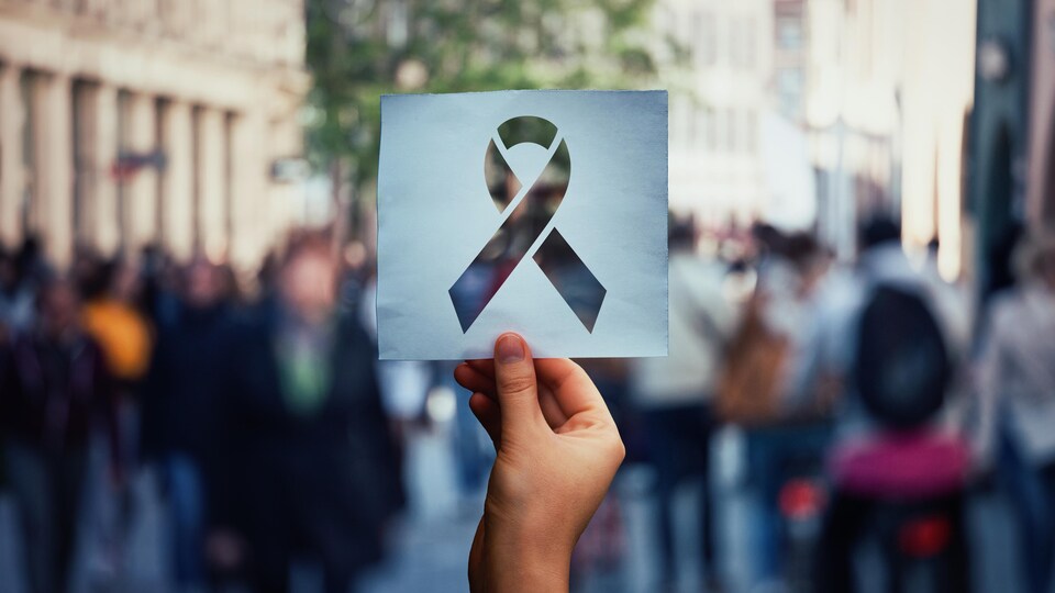 Une main tient une feuille de papier avec le symbole du ruban rouge de la lutte contre le VIH.