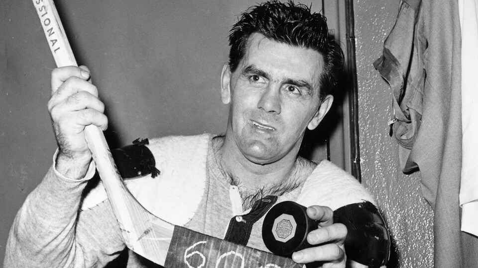 Maurice Richard tenant un bâton de hockey et une rondelle dans ses mains.