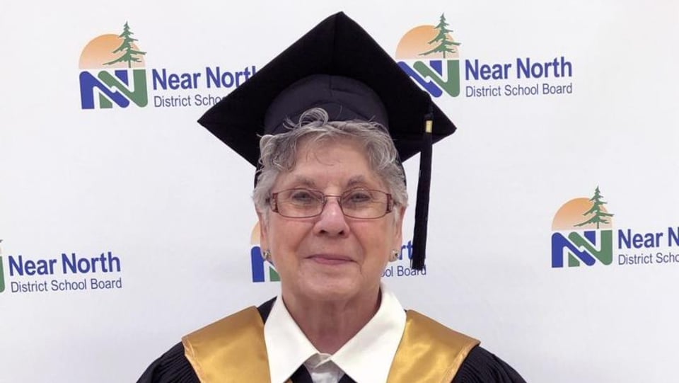 Une dame âgée vêtue d'une toge de finissante tient son diplôme d'études secondaires dans ses mains.
