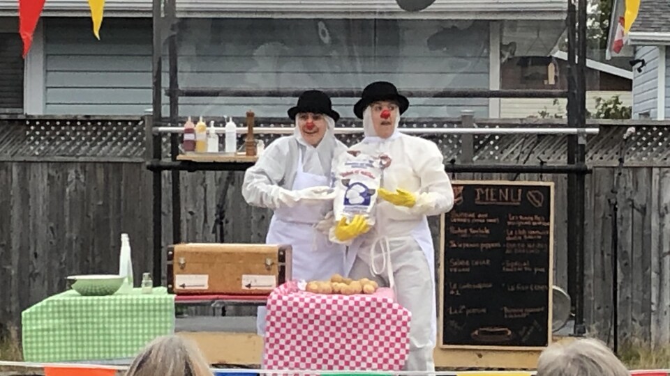 Deux clowns portant des chapeaux melon présentent un sac de pommes de terre au public.