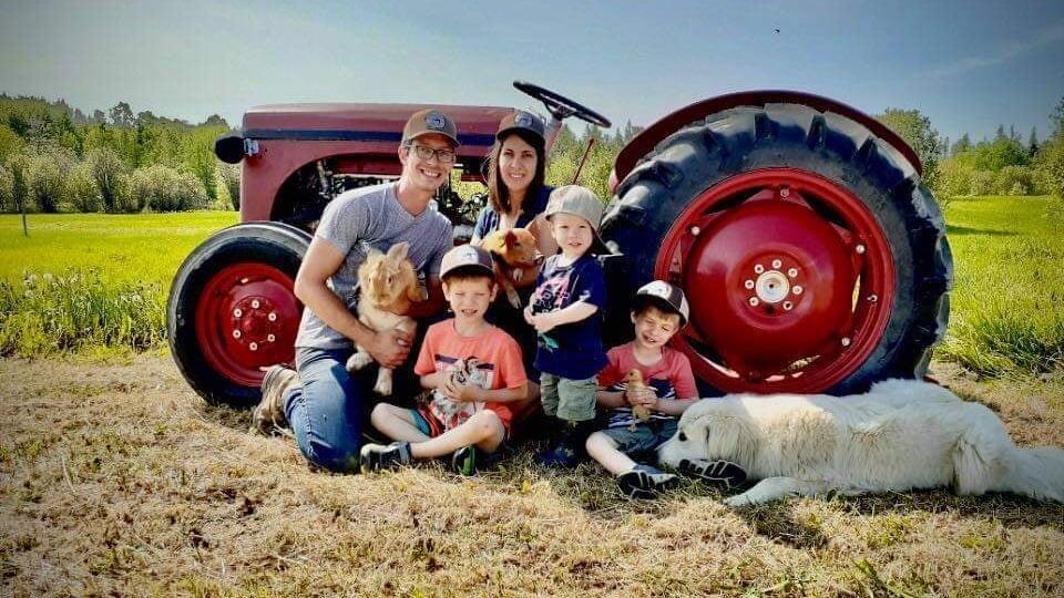La famille devant un tracteur en compagnie de leur chien, un lapin, un cochon, une caille et un caneton.
