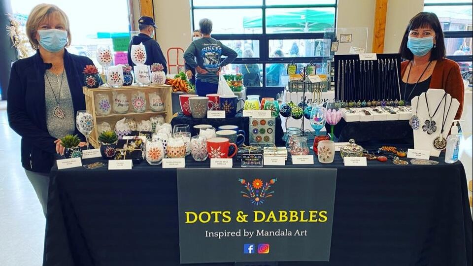 Les deux femmes sont debout de chaque côté de leur table de produits artisanaux.